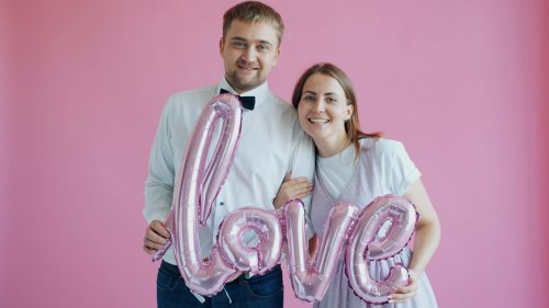 Couple holding pink 'love' balloons on pink background