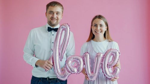 Couple holding pink balloons spelling the word love
